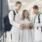 A group of medical students in white coats studying together in a hospital hallway.