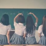 Group of teenage girls in school uniforms enjoying time together in a classroom, posing with playful gestures.