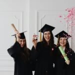 Three young female graduates celebrating indoors with diplomas and confetti.