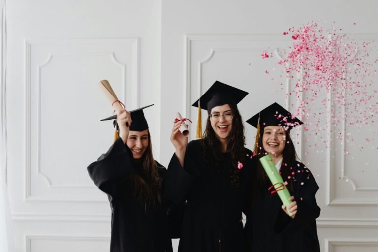 Three young female graduates celebrating indoors with diplomas and confetti.