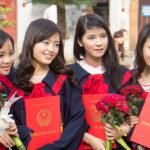 Four graduates in gowns holding diplomas and flowers