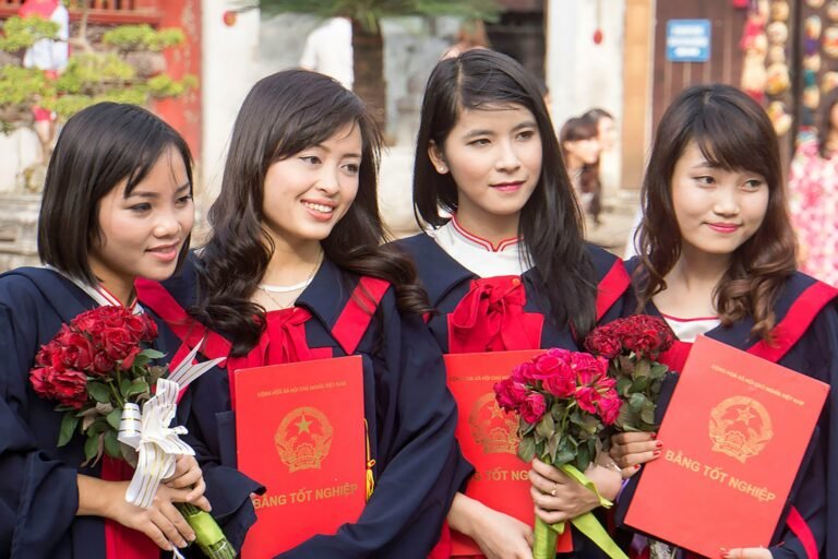 Four graduates in gowns holding diplomas and flowers
